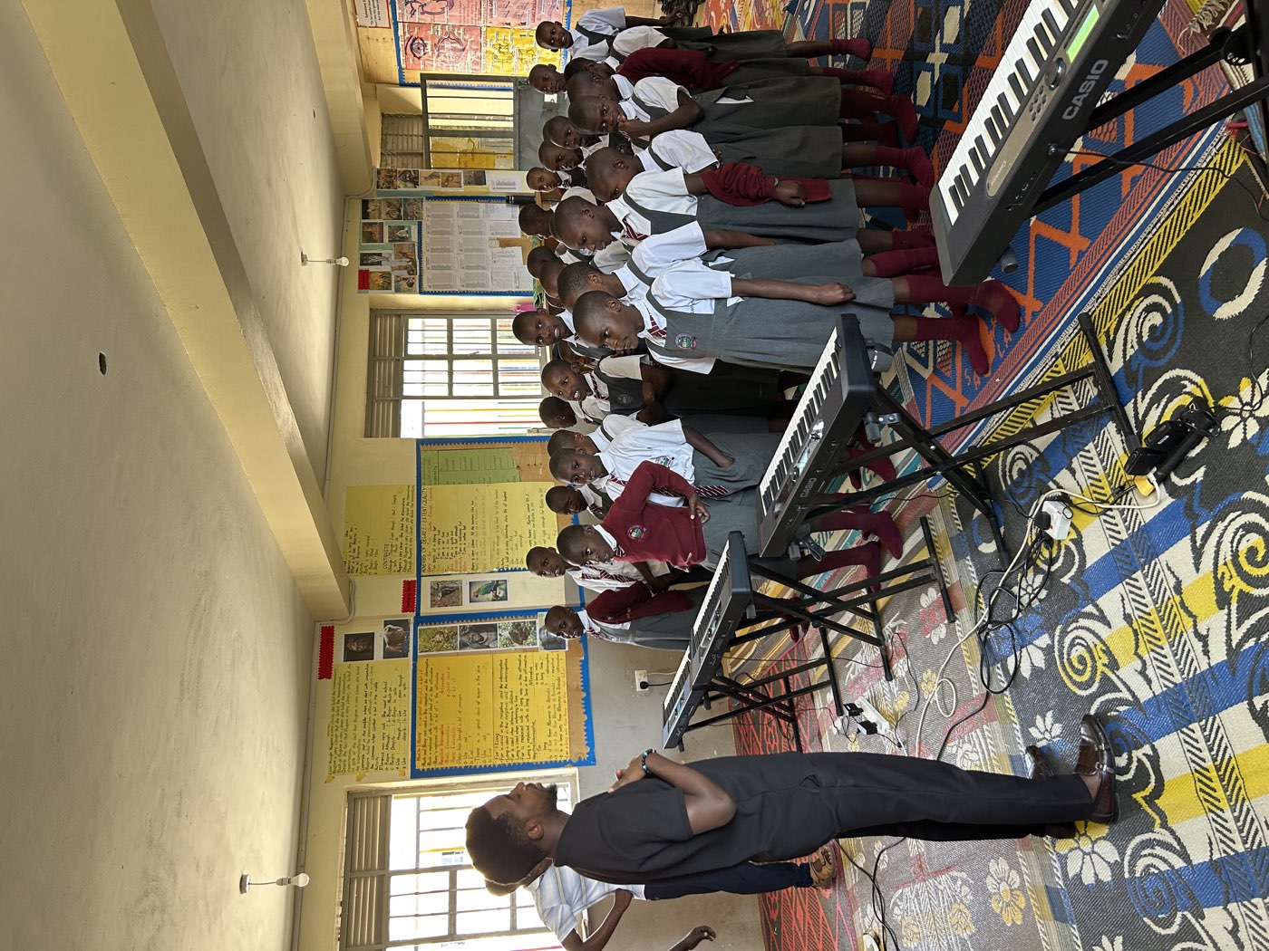 A teacher leads a class of pupils standing at keyboards