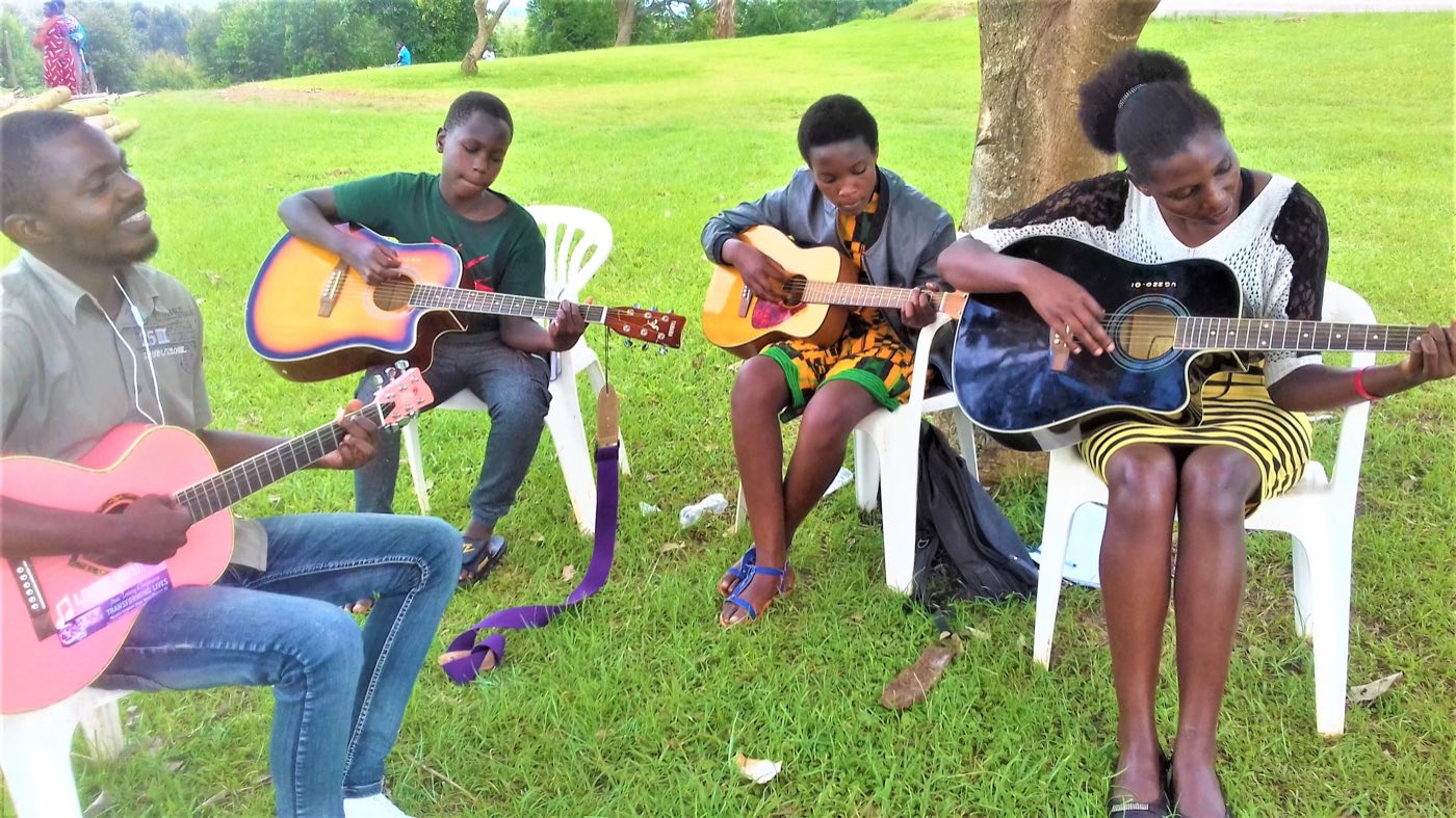 Young people learning guitar on plastic chairs on a lawn