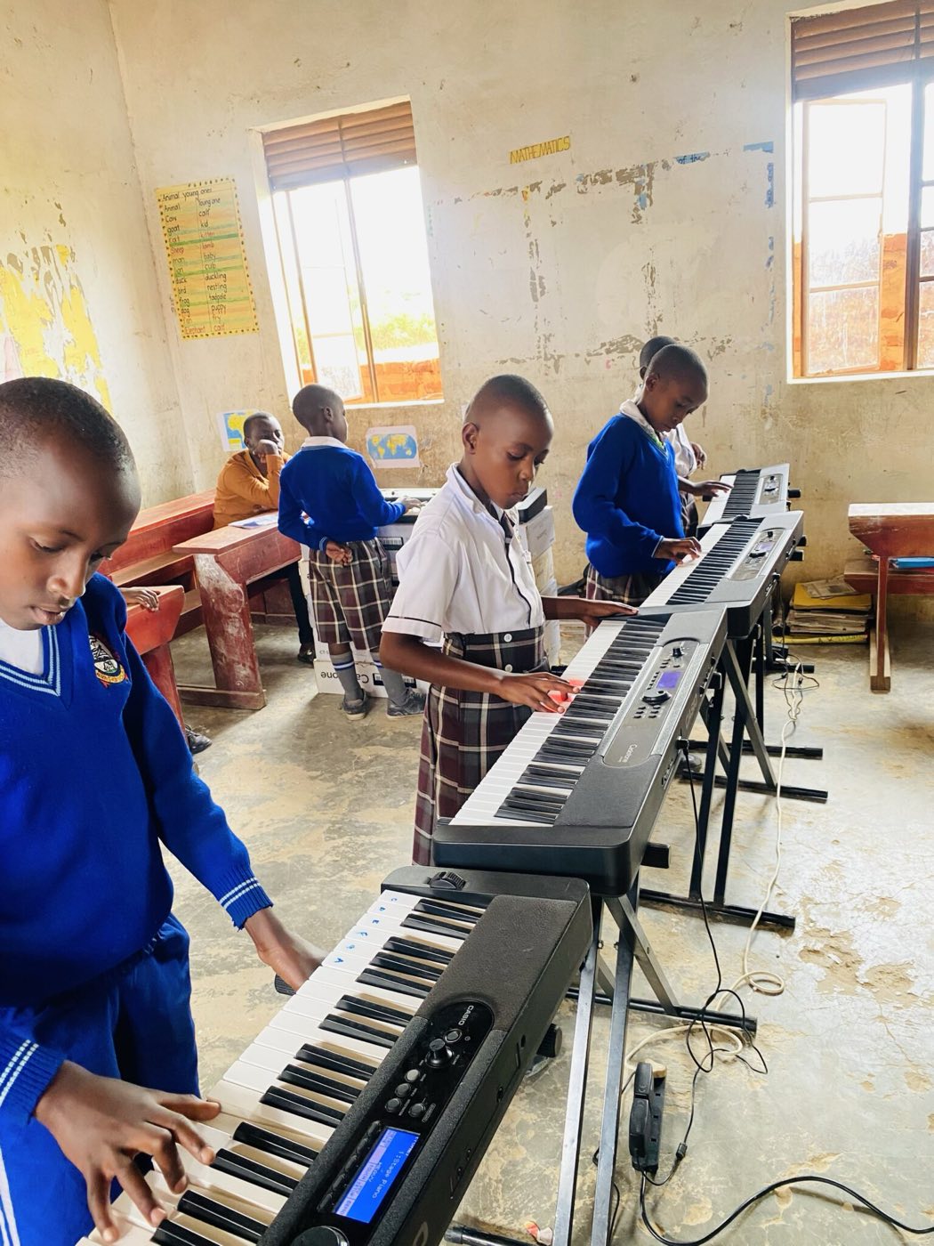 Pupils in school uniform practising on a row of keyboards in a classroom